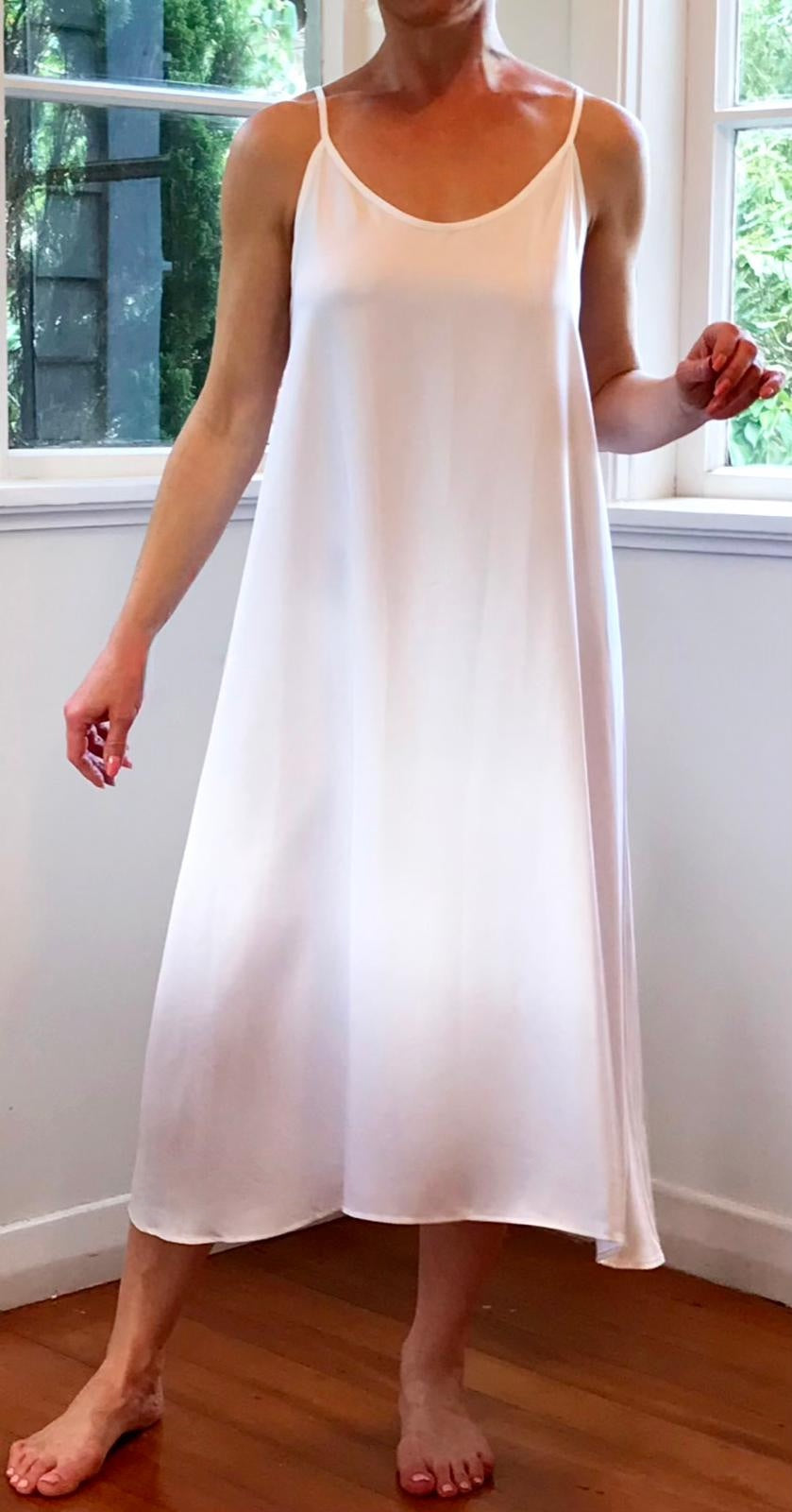 Person wearing a white slip dress standing in a room with windows.