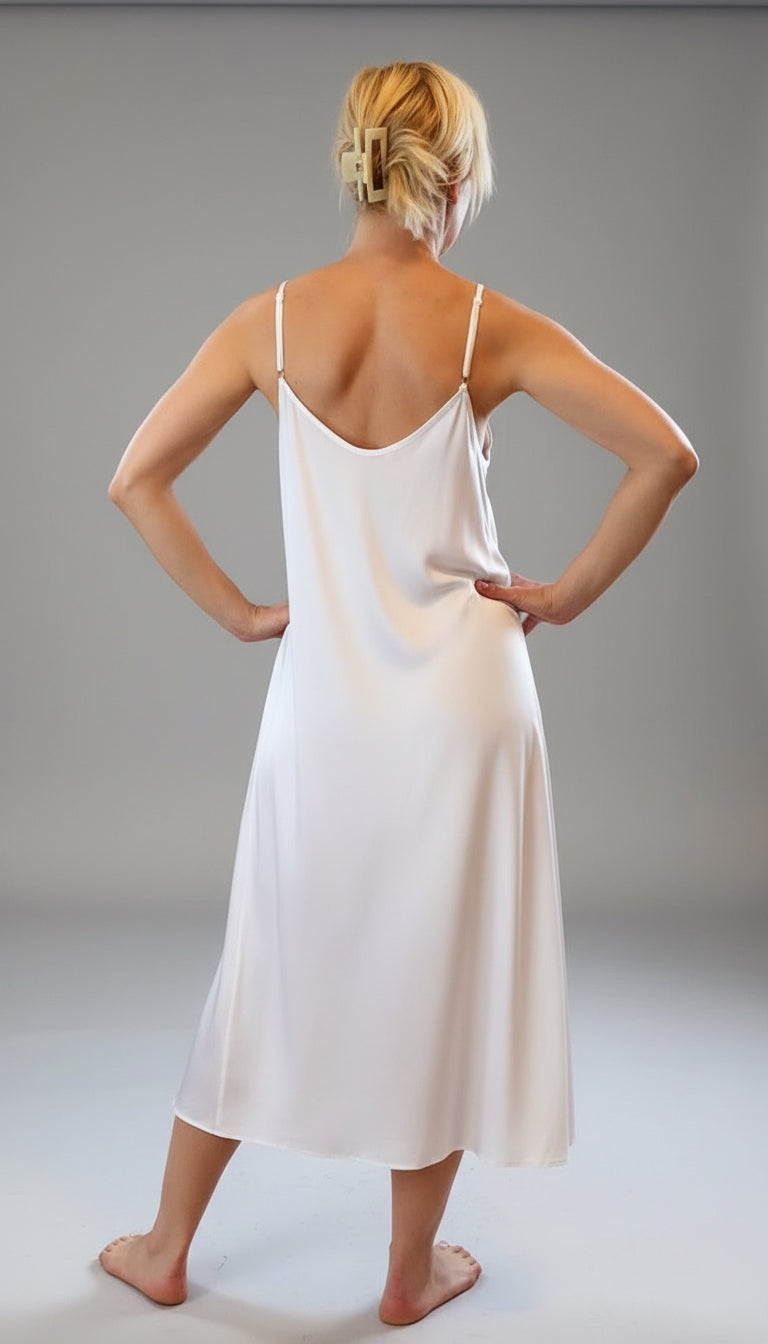 Woman wearing a white slip dress standing in a room with large windows.