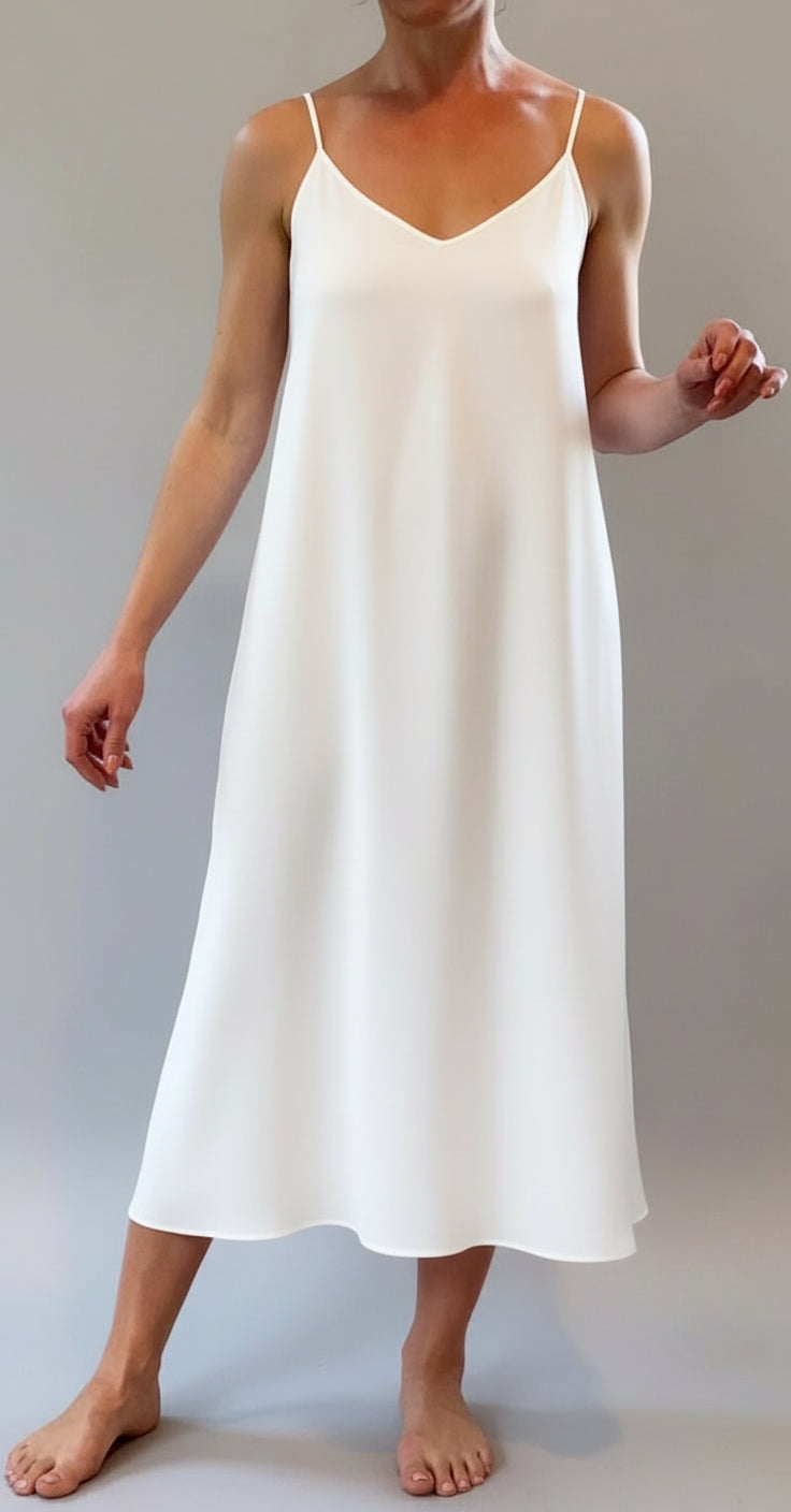 Person wearing a white slip dress standing in a room with windows.