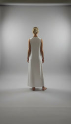 Woman wearing a white dress standing in a room with wooden floor and large windows.