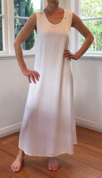 Person wearing a white dress standing in a room with large windows.