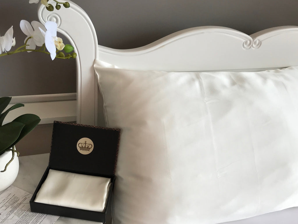 White silk pillow on a bed with a black jewelry box and orchid in the foreground.