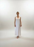 Woman in a white dress standing in a room with large windows and wooden flooring.