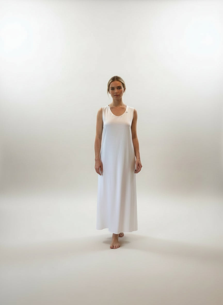 Woman in a white dress standing in a room with large windows and wooden flooring.