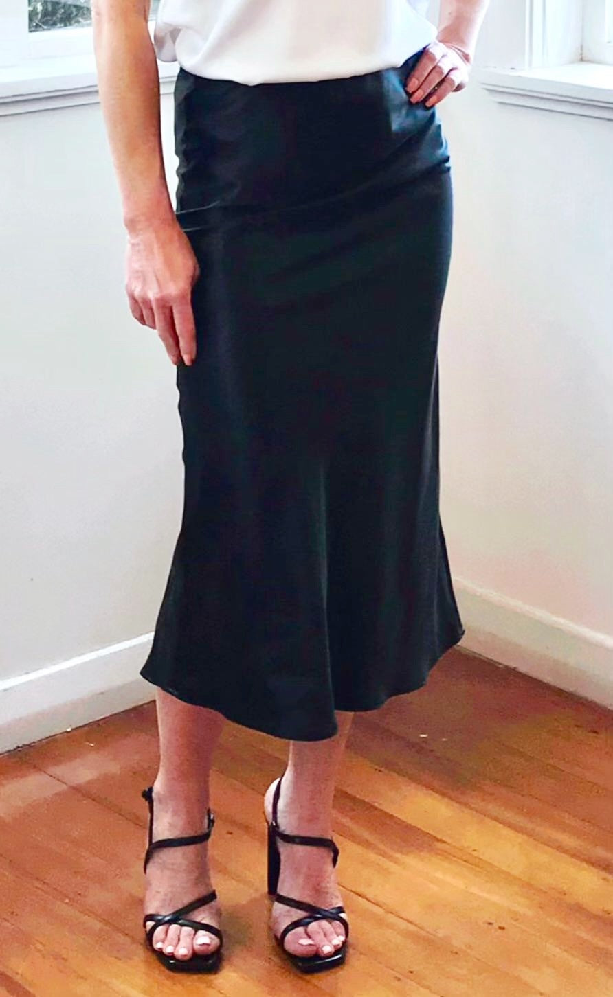 Person wearing a black skirt and white top indoors on a wooden floor.