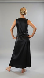 Person wearing a black sleeveless dress standing in a room with large windows.