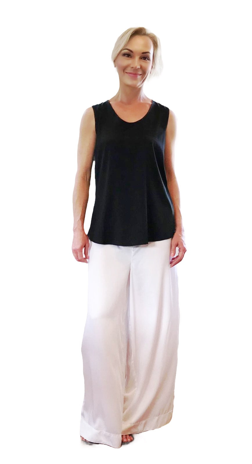 Woman wearing a black sleeveless top and white pants on a white background